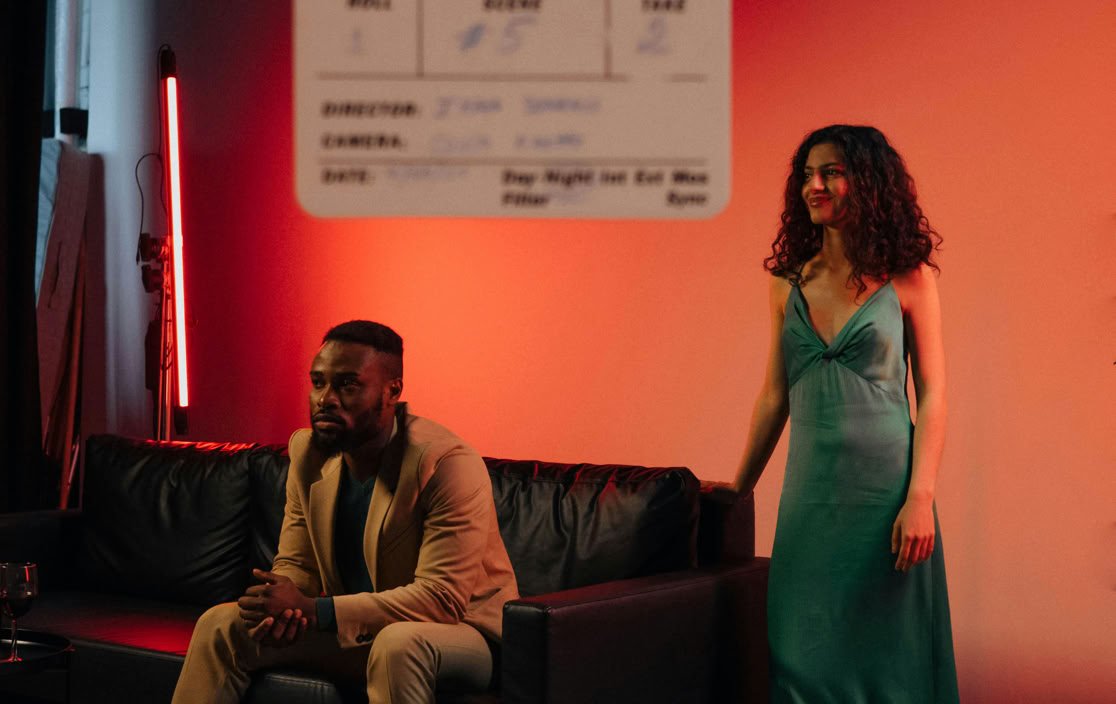 Two actors on a film set with dramatic lighting and a clapboard.